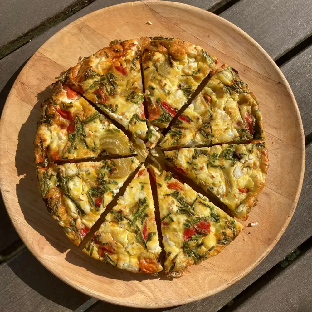 A golden vegetable frittata cut into slices on a wooden board